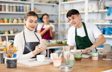 Fototapeta premium Young woman and young man sculpting ceramic product in workshop