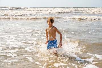 Fototapeta na wymiar Youth Child Preteen Boy Running Into the Waves and Ocean Water at the Sunny Beach