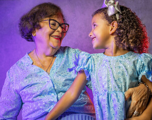 Studio portrait of grandmother with granddaughter wearing beautiful blue dresses with purple lighting in the background