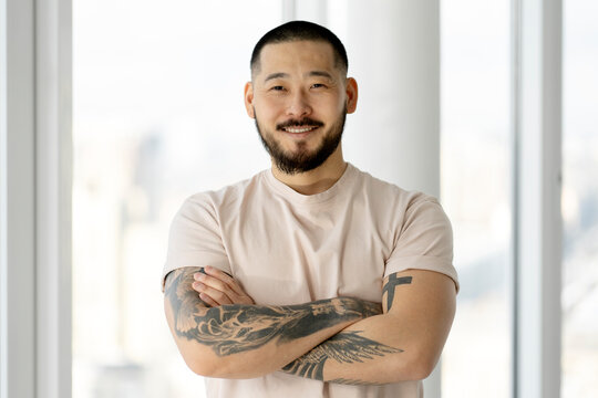 Portrait of handsome smiling Asian man with arms crossed and stylish tattoos looking at camera - Powered by Adobe