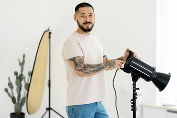 Portrait of professional Korean photographer with tattooed hands, holding camera equipment,...