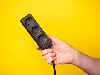 A hand holds a power. No face, yellow background.
