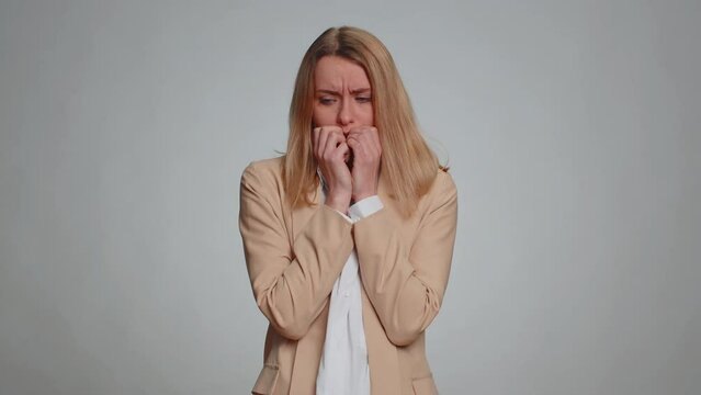 Upset scared frightened businesswoman biting nails, feeling worried nervous about serious troubles, stress and anxiety disorder, panic attack, guilty. Female girl in suit. Woman on gray background
