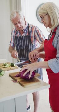 Vertical video of senior caucasian couple preparing food in kitchen, slow motion