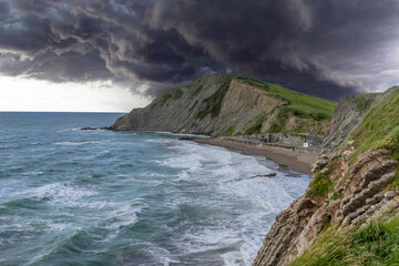 The storm is approaching on the green grassy ridges forming Flysch on the rocks on a summer day in Zumaia. Basque. Spain