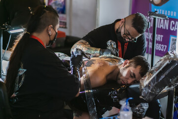 man with a gesture of pain due to a tattoo made by a man and a woman tattoo artists, use of biosafety elements, art fusion