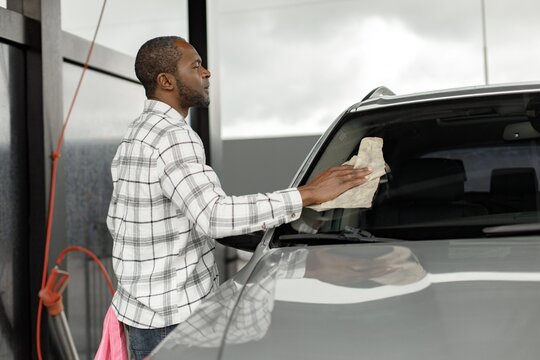 Middle aged black man wiping his car with a rag outside in the car wash