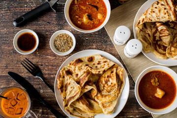 Malaysian Cuisine Roti Canai - Crispy Indian style pancake served with curry chicken dipping sauce with Thai ice tea on wooden table.