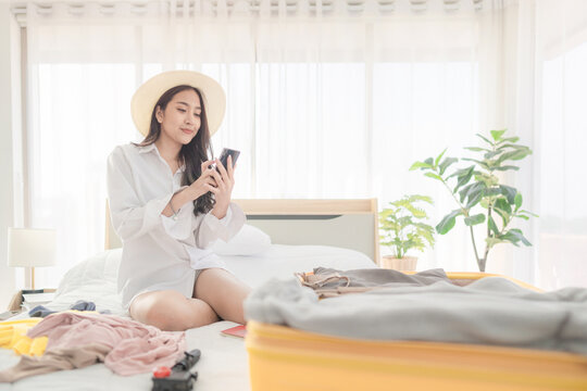 Asian Young woman checking tickets and passports on smarthphone sitting with suitcase on the bed. Prepairing for the summer vacations. Prepairing for the summer vacations.