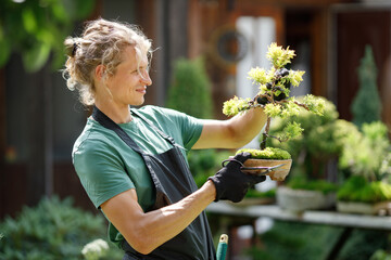 Young blonde man pruring bonsai at backyard garden