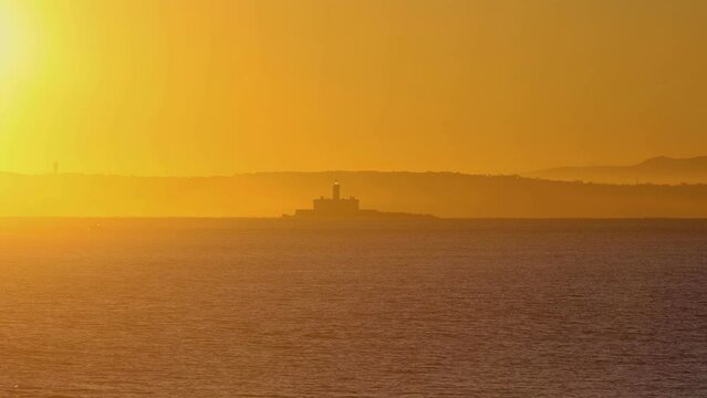 wide and amazing view of Bugio lighthouse with huge sunrise, on a rocky island, on the atlantic ocean, on a sunny day, near the Oeiras coast and Tejo river, in Lisbon, Portugal