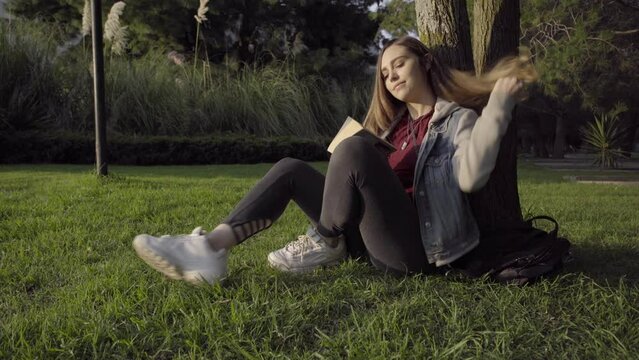 Mujer joven se sienta debajo de un arbol para leer durante el atardecer.