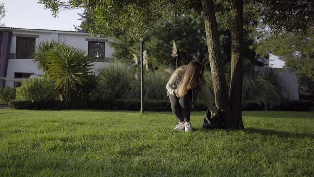 Mujer joven se sienta debajo de un arbol para leer un libro durante el atardecer.