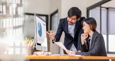 Team of confident Asian business people point to graphs and charts to analyze market data, balance...