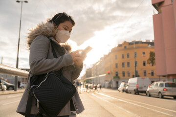 asia female woman wear face mask virus protection while using smartphone street sidewalk sunset waiting for taxi or bus that she booking from smartphone city service application online while travel