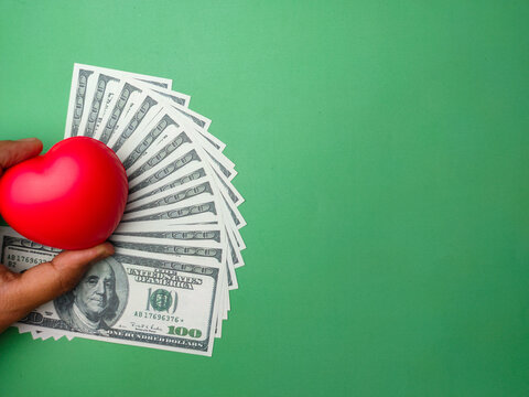 Hand holding red heart with banknotes on green background