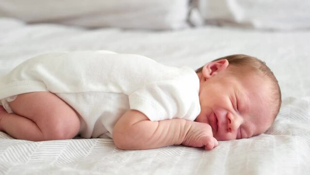 Cute adorable newborn baby boy lying on stomach on white bed at home sleeping, awaking, moving. Purity,innosence concept.Full body,