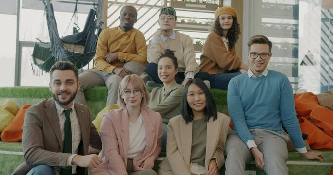Multinational group of young people sitting in creative coworking space smiling looking at camera. Business people and modern office concept.