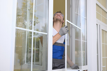An experienced master holds a mosquito net in his hands, looks up installing it on the window. Qualified installer puts a protective net against insects on the window