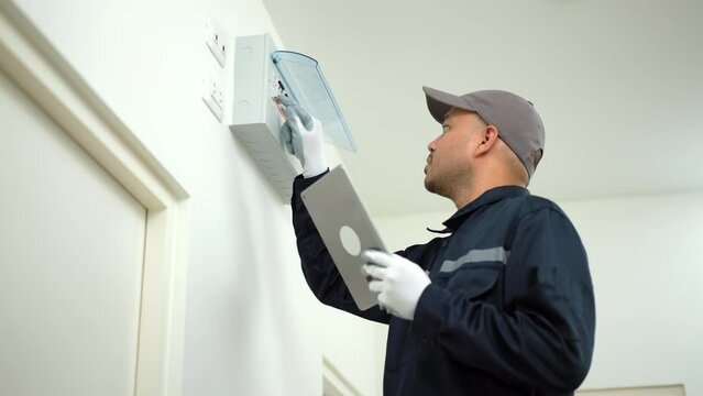 Electrician man in uniform using tablet for maintenance or fixing switches sockets  circuit breaker ,electrical system. Technician fixing an electric fuse at home. Home service concept.