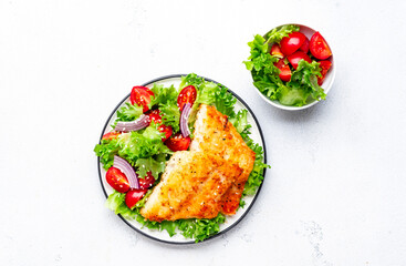 Fried cod fish with salad garnish from lettuce, cherry tomatoes and red onion with sesame seeds, white table background, top view