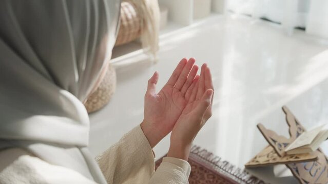 Close-up Asia muslim woman hand pray doa communicate to allah wear prayer clothes green mukena cover hijab in living room at home, pray room bright light, Islamic faith, Ramadan Kareem, Eid Mubarak.