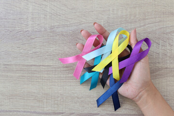 World cancer day background. Colorful ribbons on palm hands on the wooden table, cancer awareness. 