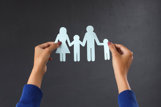 Close-up hands holding family figure  over dark gray background. Family insurance and medical care concept. 