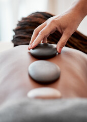 Black woman, hands and rock on back in spa treatment for relaxation, stress relief or massage at resort. Hand of masseuse applying rocks to African American female in physical therapy for wellness