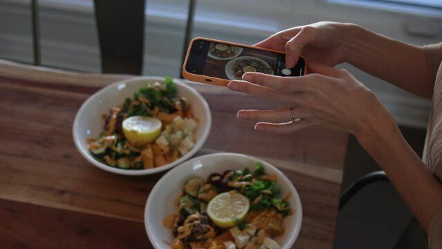 female photographer lines up smartphone picture of vegetarian vegan food bowls - from above