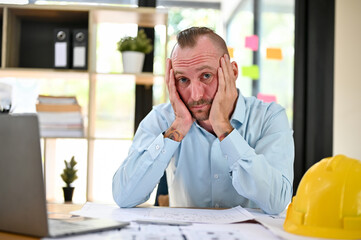 Fototapeta premium Bored and tired caucasian male engineer hands on his chin, looking at the camera