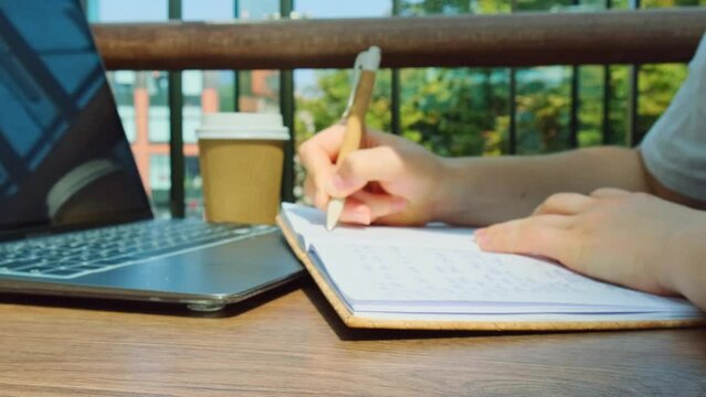 Unrecognizable Young woman study at wooden table in shopping mall food court. Drinking coffee from paper cup. Student making homework Female hands writing on notebook gratitude journal self reflection
