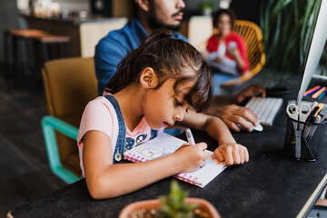 Hispanic child daughter doing homework, drawing and painting with her father and family in background at home in Mexico Latin America, home office concept