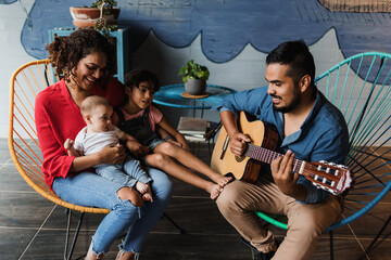 Fototapeta na wymiar hispanic father playing guitar, singing and having fun with his family and daughter at home in Mexico Latin America