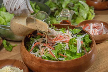 woman chef mix fresh baby cos salad and pour salad dressing in glass blow. Organic Vegetables mix all green salad In glass bowl. Breakfast fresh salad and clean vegetable.