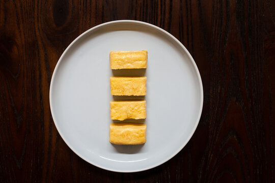 Tamagoyaki on a white plate on a dark brown wooden board