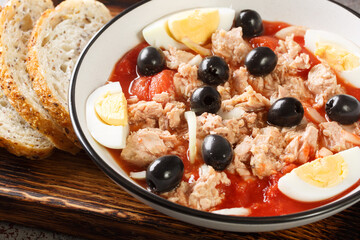 Traditional Murcian Salad Mojete made of tomato, canned tuna, black olive, boiled egg and onion closeup on the plate on the wooden board. Horizontal