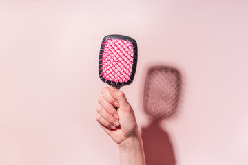Pink comb in female hand under hard light against pink background.