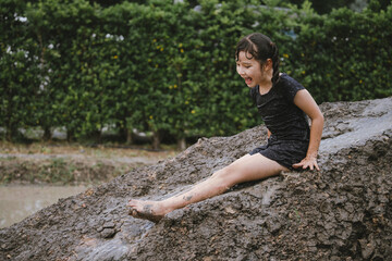 Little girl has fun with soil and mud slider in public playground and show happiness with smiling.