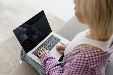 Young IT woman in casual clothes hold use work on blank screen laptop pc computer sit on grey sofa couch stay at home hotel flat rest relax spend free spare time in living room People lounge concept