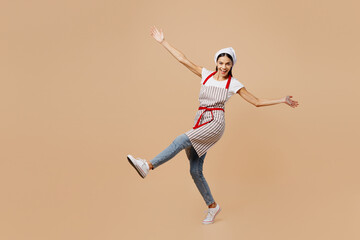 Fototapeta na wymiar Full body young happy housewife housekeeper chef baker latin woman wear apron toque hat walk go with outstretched hands look camera isolated on plain pastel light beige background. Cook food concept.
