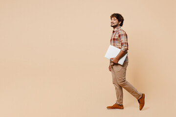 Full body side view young IT Indian man wear brown shirt casual clothes hold closed laptop pc...