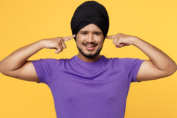 devotee Sikh Indian man ties his traditional turban dastar wear purple t-shirt cover ears with...