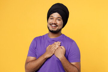 Smiling greatful devotee Sikh Indian man ties his traditional turban dastar wear purple t-shirt put...