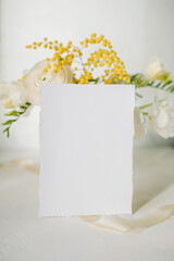 white paper mockup with texture on festive peach background with flowers white and yellow colors,wedding invitation mockup, top view, spring mockup