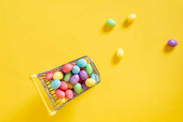  Happy easter.Shopping cart with colorful glitter easter eggs on the yellow background.Top view
