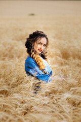 Naklejka na ściany i meble Beautiful Ukrainian young woman standing alone in a yellow wheat field. The brunette looks at the camera hugging the spikelets of wheat. Peaceful happy Ukraine.