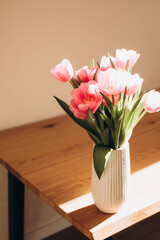 Gently pink bouquet of tulips in a white vase on wooden table. Spring background with a bouquet of flowers. Top view