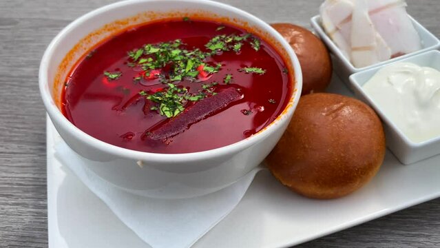 Traditional Ukrainian borscht soup with bread pampushki buns, lard salo cured pork fat and sour cream, soup with beetroot and beef, 4K shot