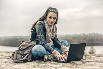 Long hair hipster brunette woman sitting on the stone with a laptop in her hands. Toned